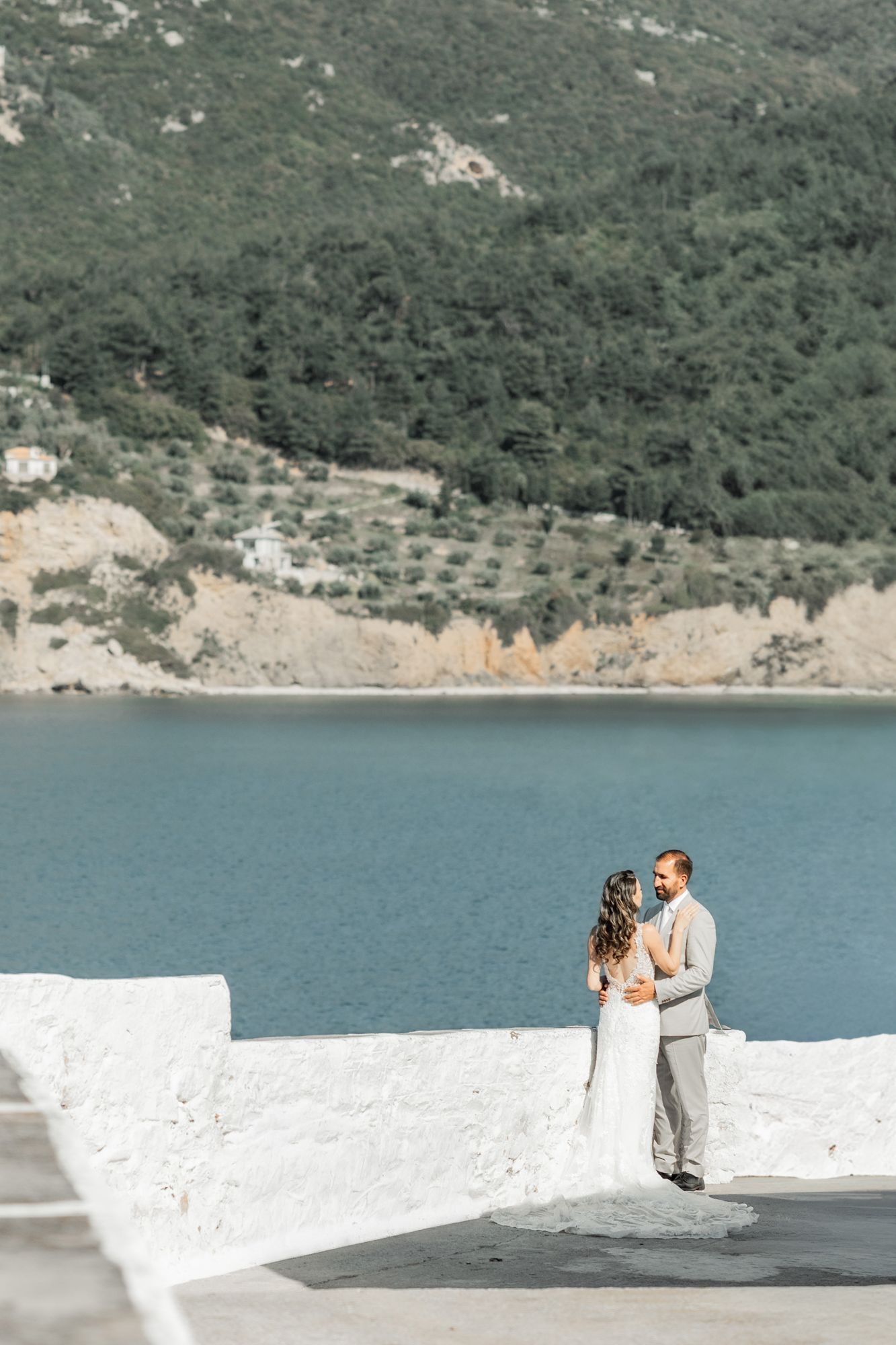 Romantic coastal wedding portrait with turquoise water and mountain backdrop.