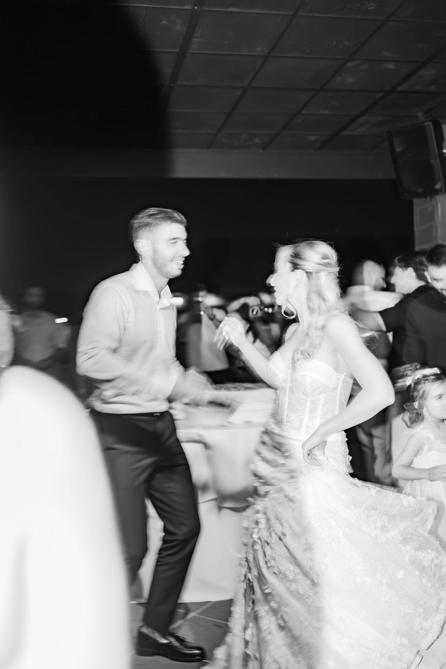 Black and white photo of a bride in a lace gown dancing with a groom at a wedding reception.