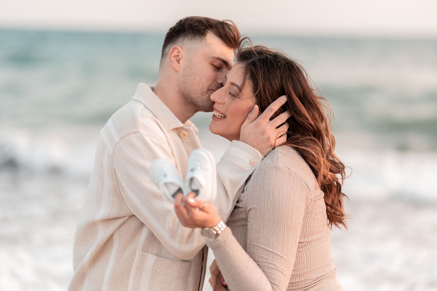 A romantic couple shares an intimate moment on the beach at sunset while holding a small white heart.