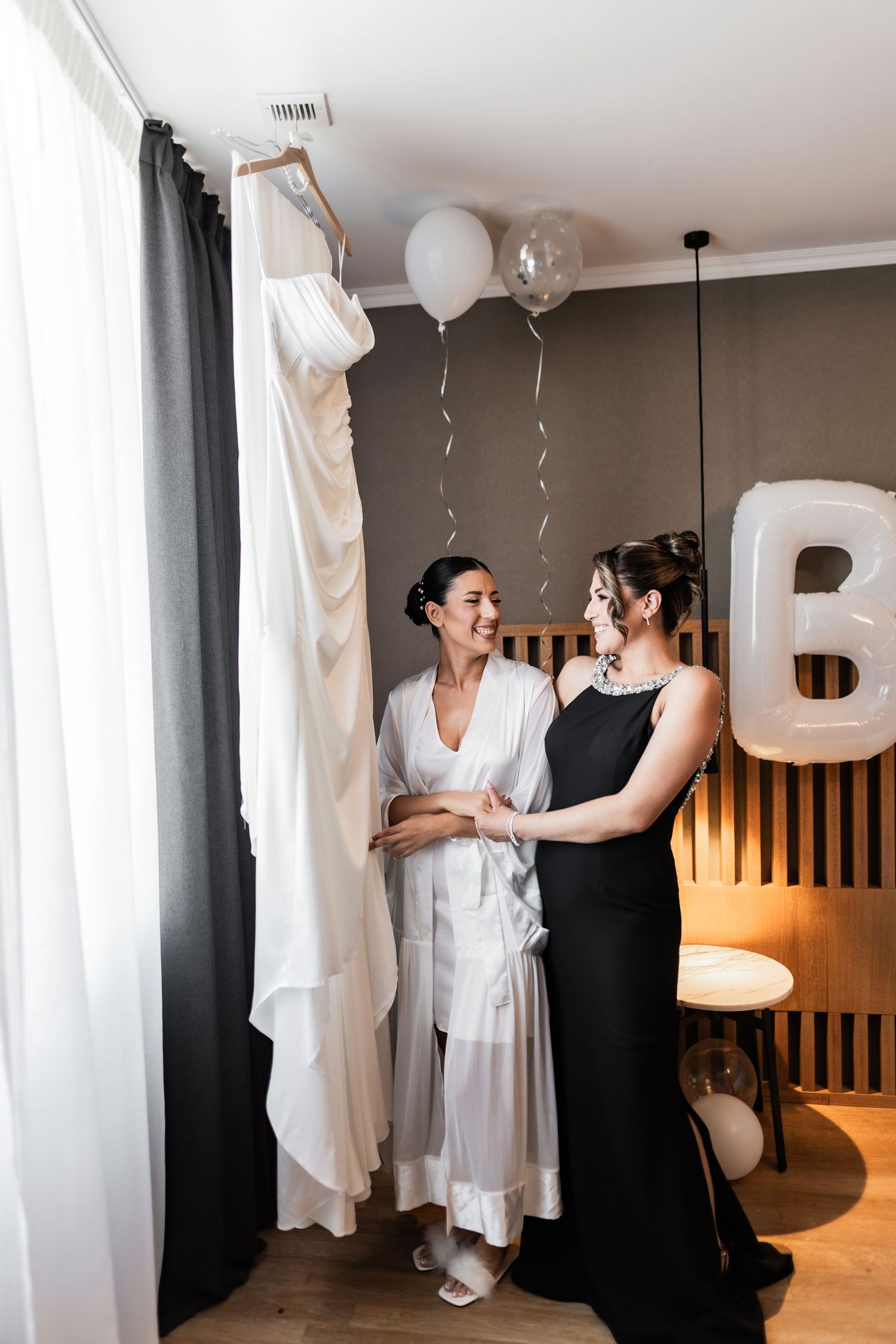 Wedding preparation scene with white dress hanging and balloons decorating a modern room.
