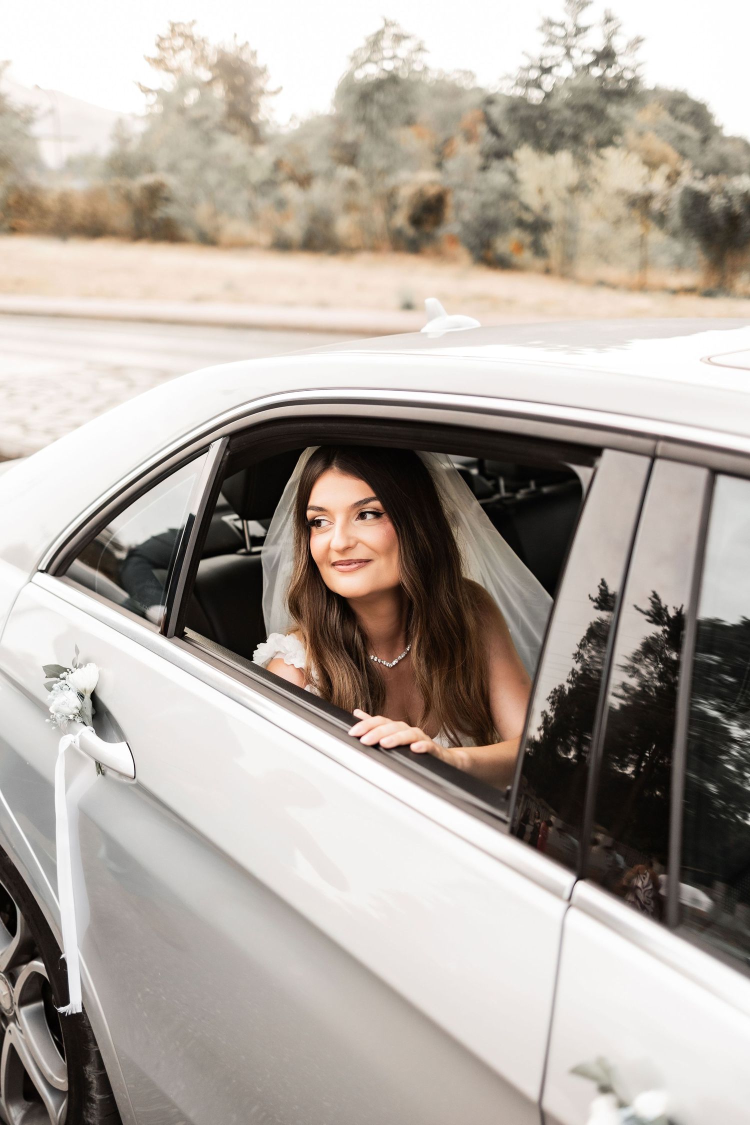 A white car with someone looking out the window during a wedding celebration.
