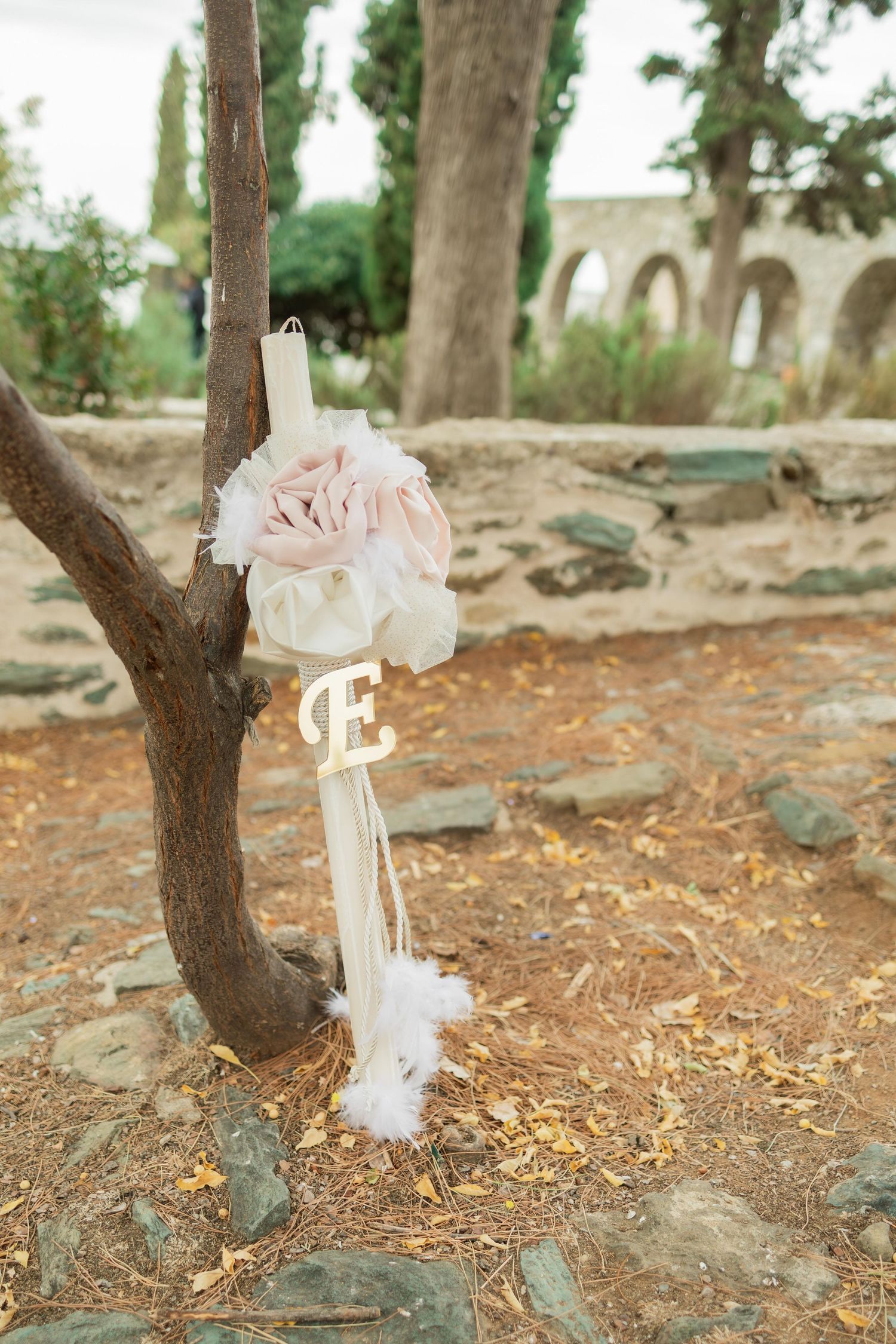 White decorative bows tied to tree trunks create an elegant outdoor wedding aisle in a rustic garden setting.
