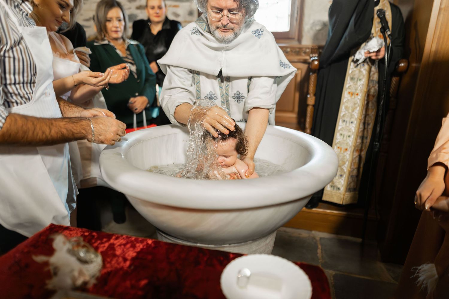 Baby being baptized in a traditional white christening gown at church ceremony.
