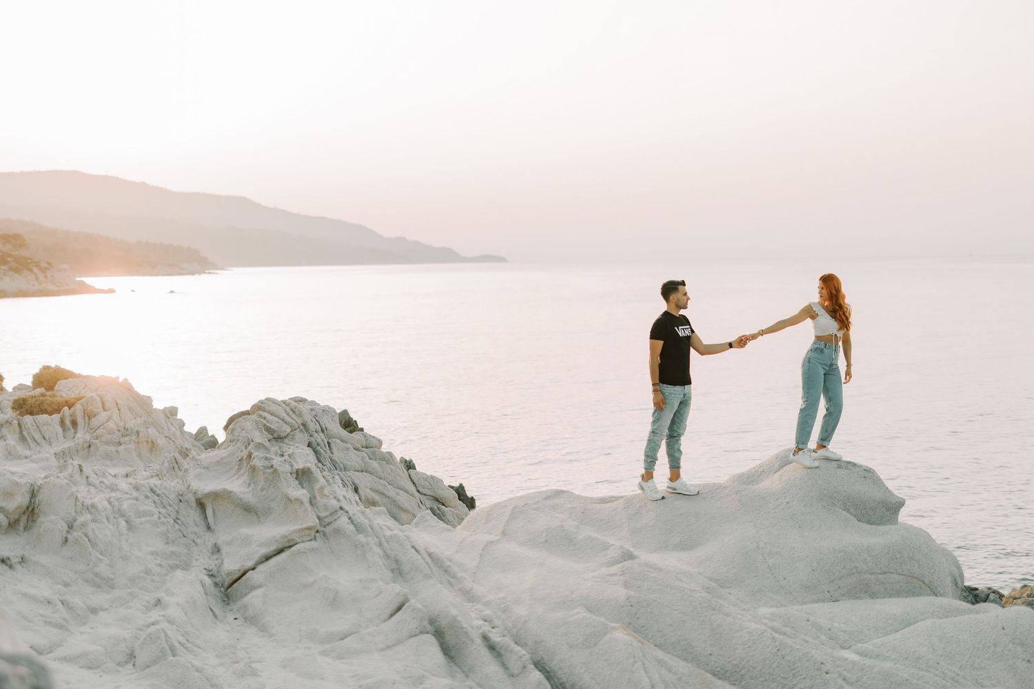 A couple stands together on white chalk cliffs overlooking a scenic coastal landscape at sunset.