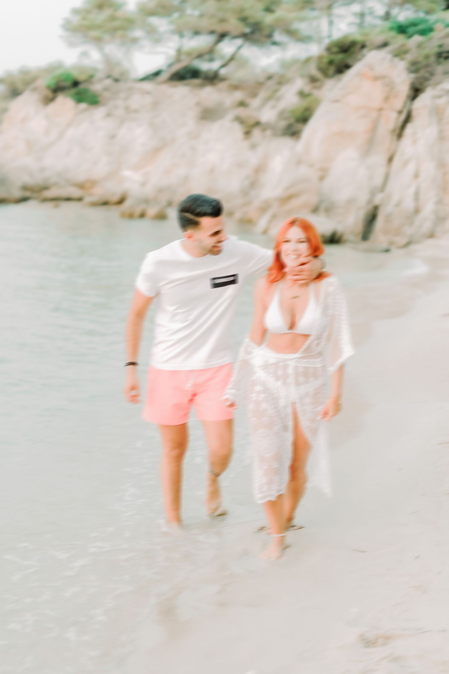 Two people playfully splashing and running through shallow ocean water on a sunny beach.