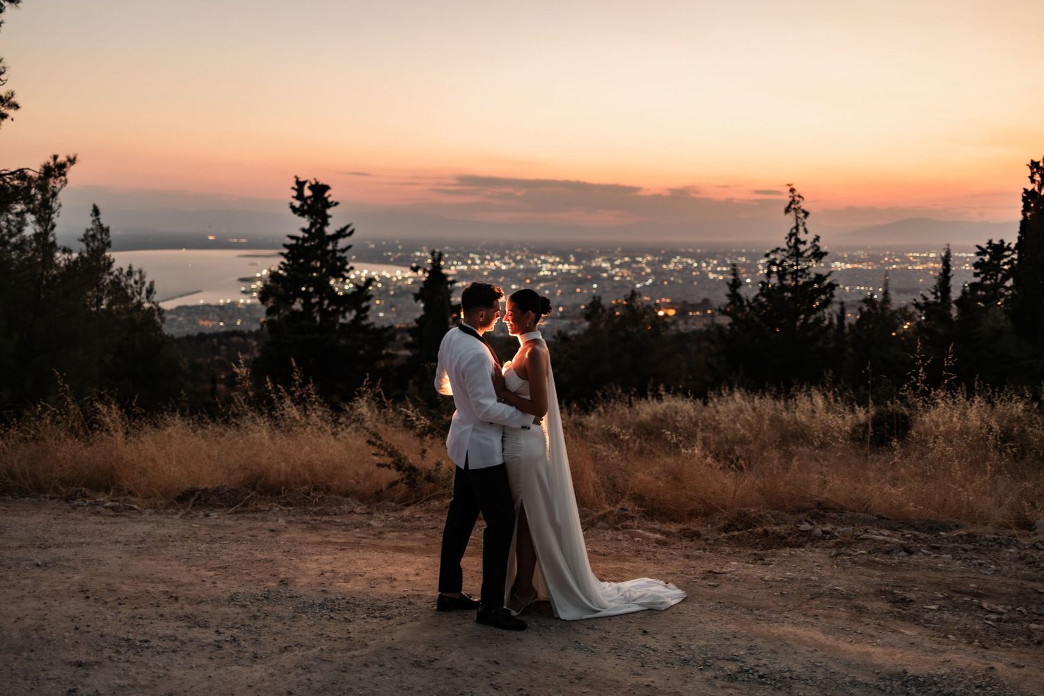Dramatic sunset wedding photos captured on mountain overlook with city lights below.