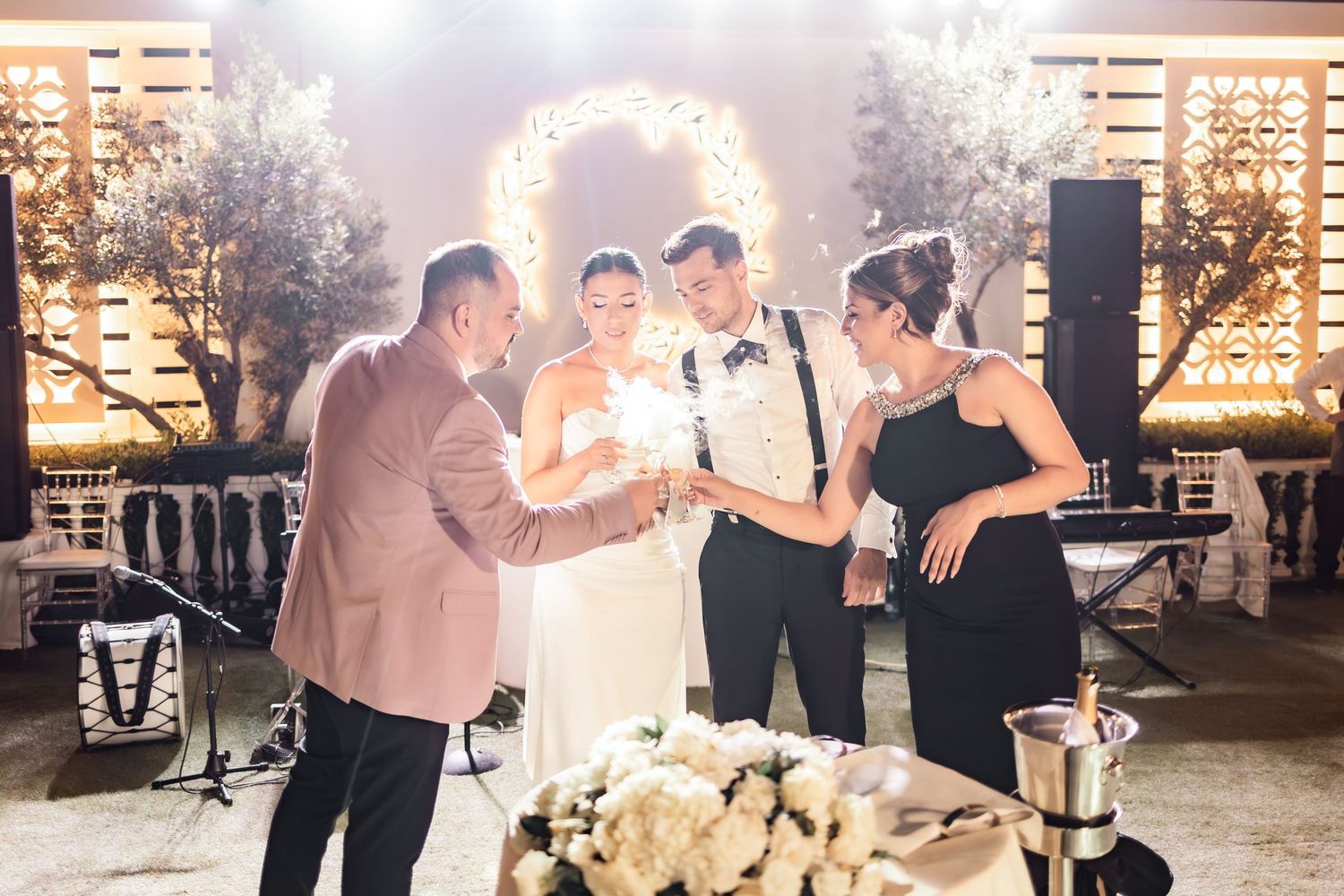 Wedding reception dance party with decorative lighting and wooden wall backdrop.