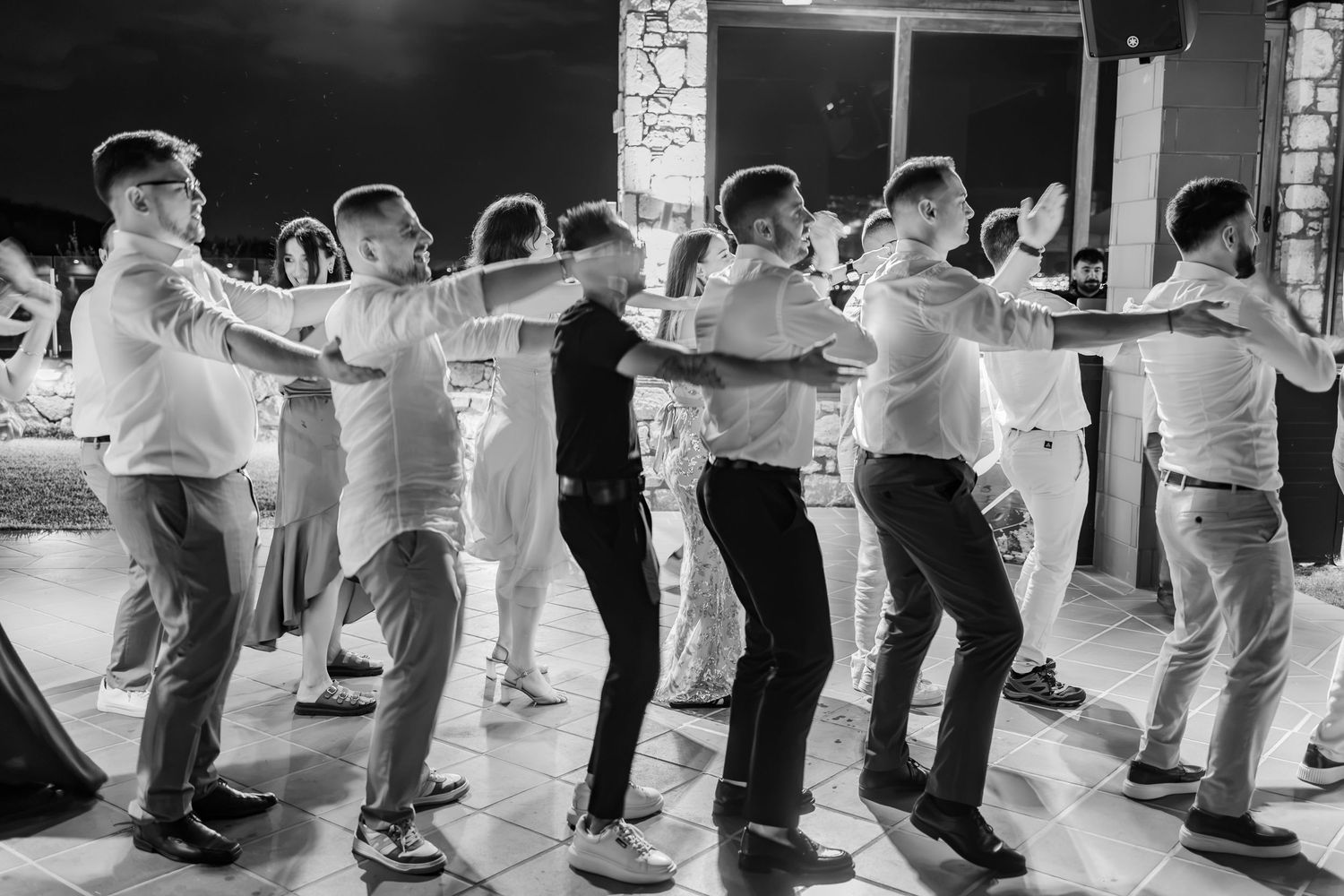 Men dancing in a line at a wedding reception in black and white photo.