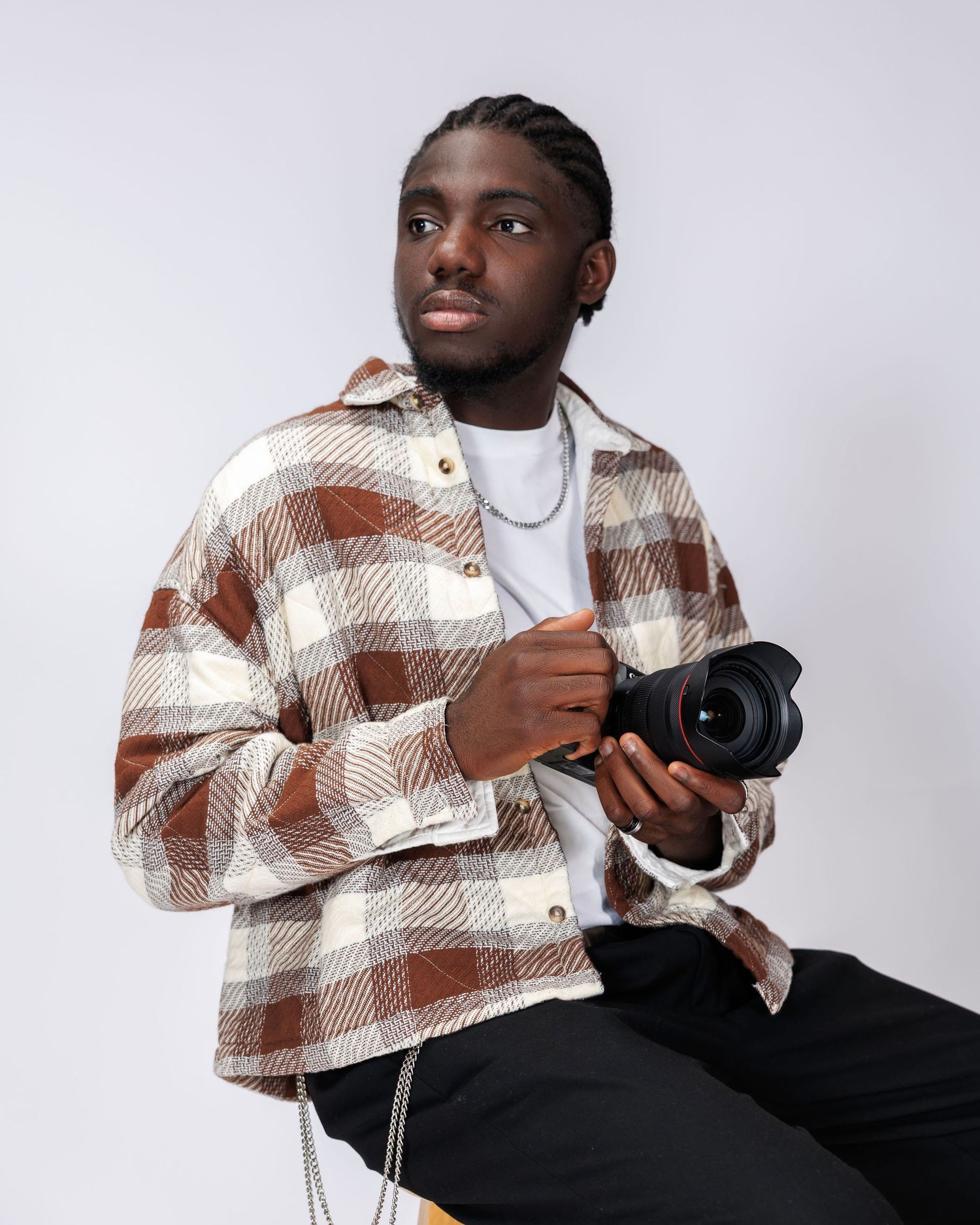 Photographer in brown plaid shirt holds camera while posing against white background.