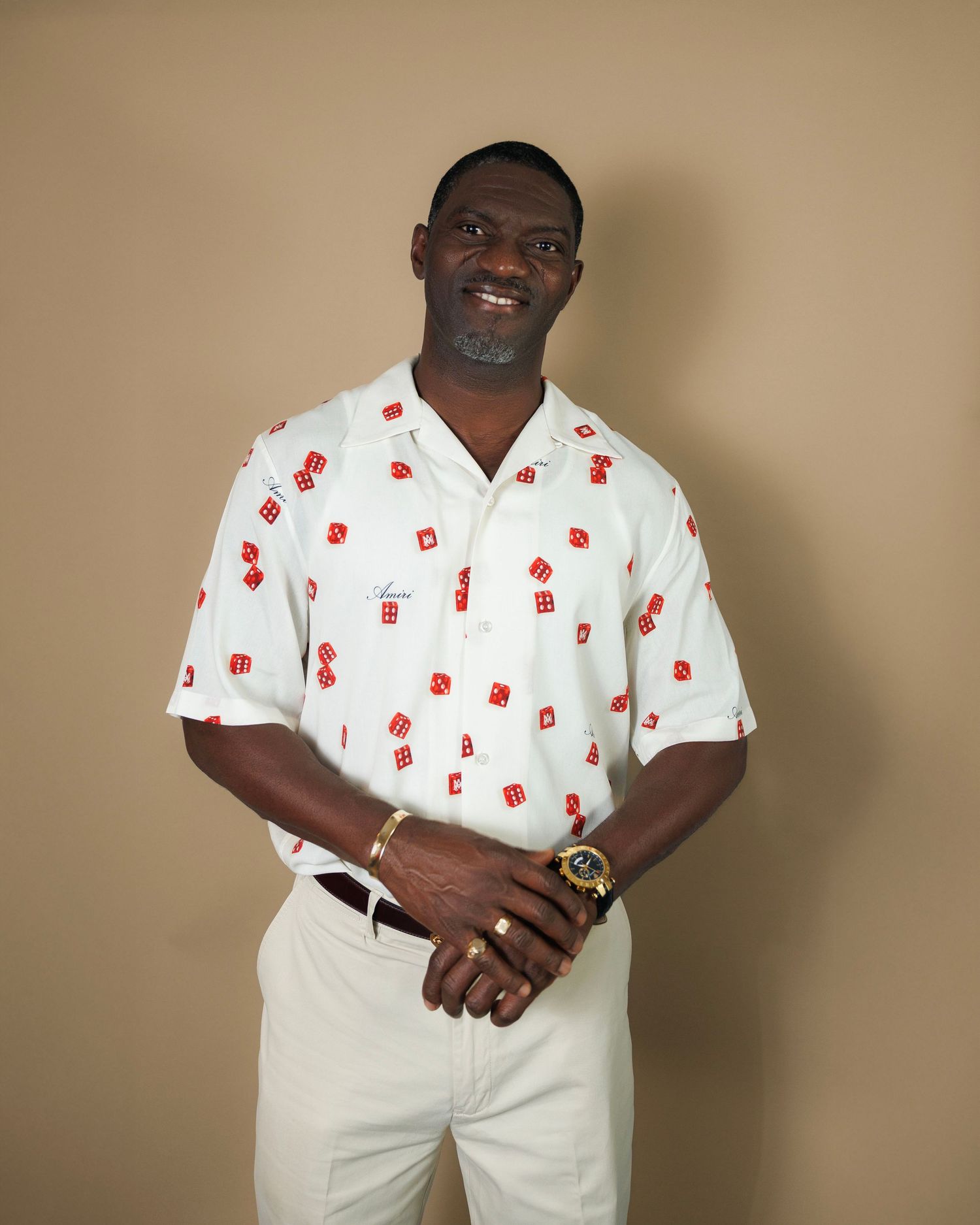 Person wearing white shirt with red pattern and khaki pants poses against beige background.