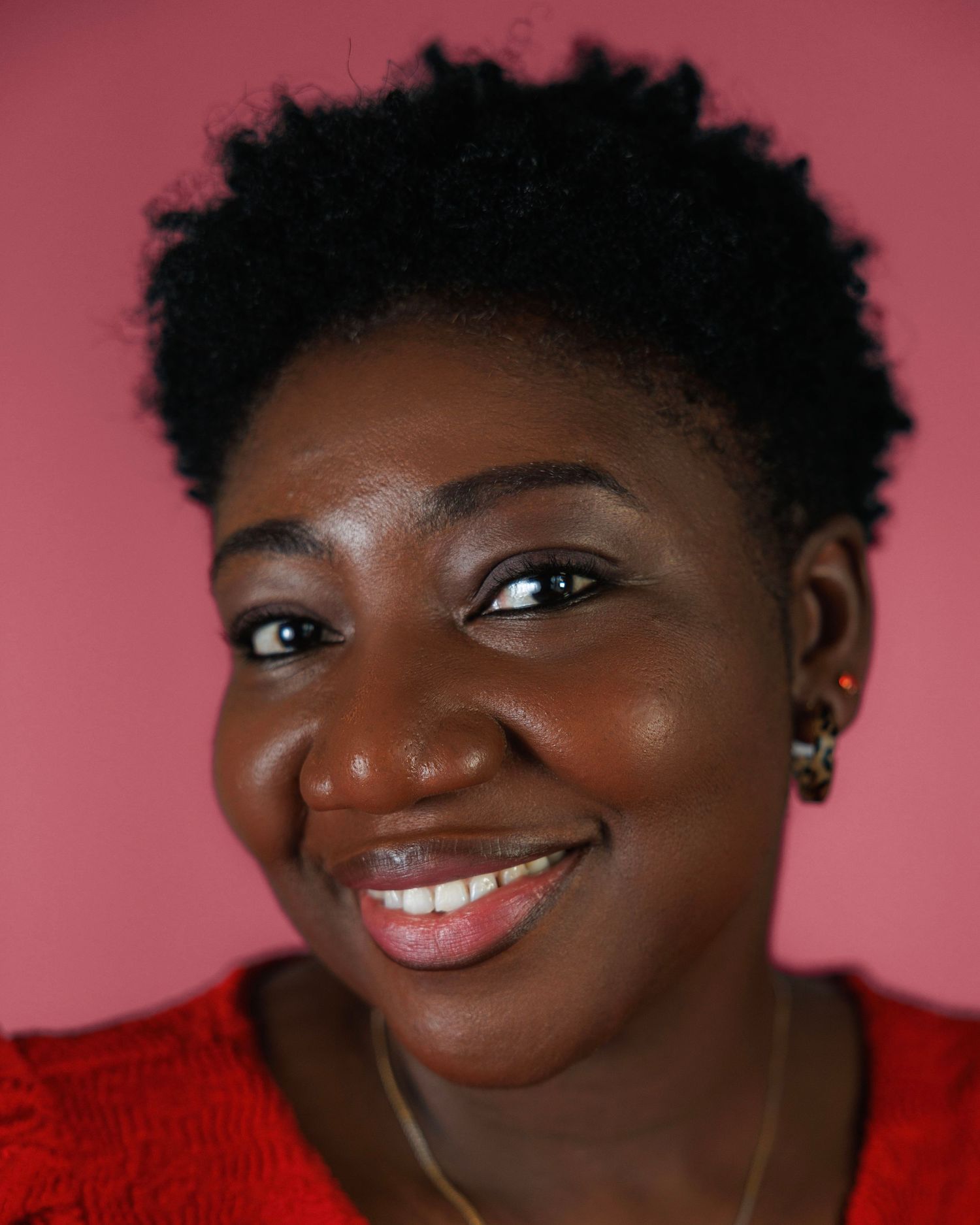 Close-up expressive poses against pink background wearing a red top.