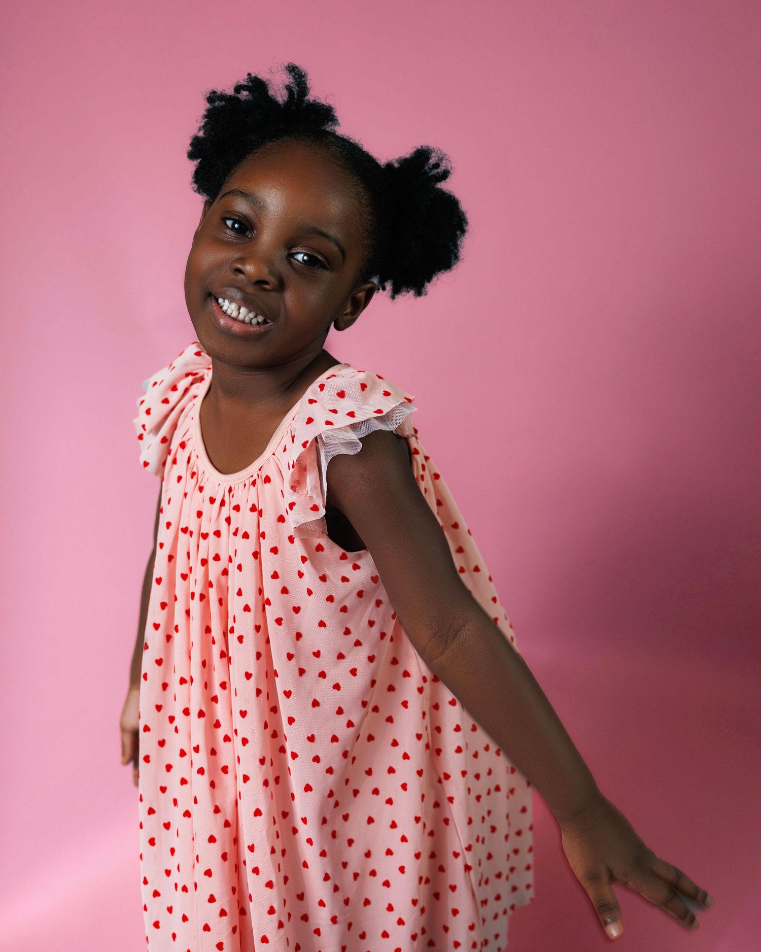 Joyful expressions and playful poses against a pink background wearing a polka dot dress.