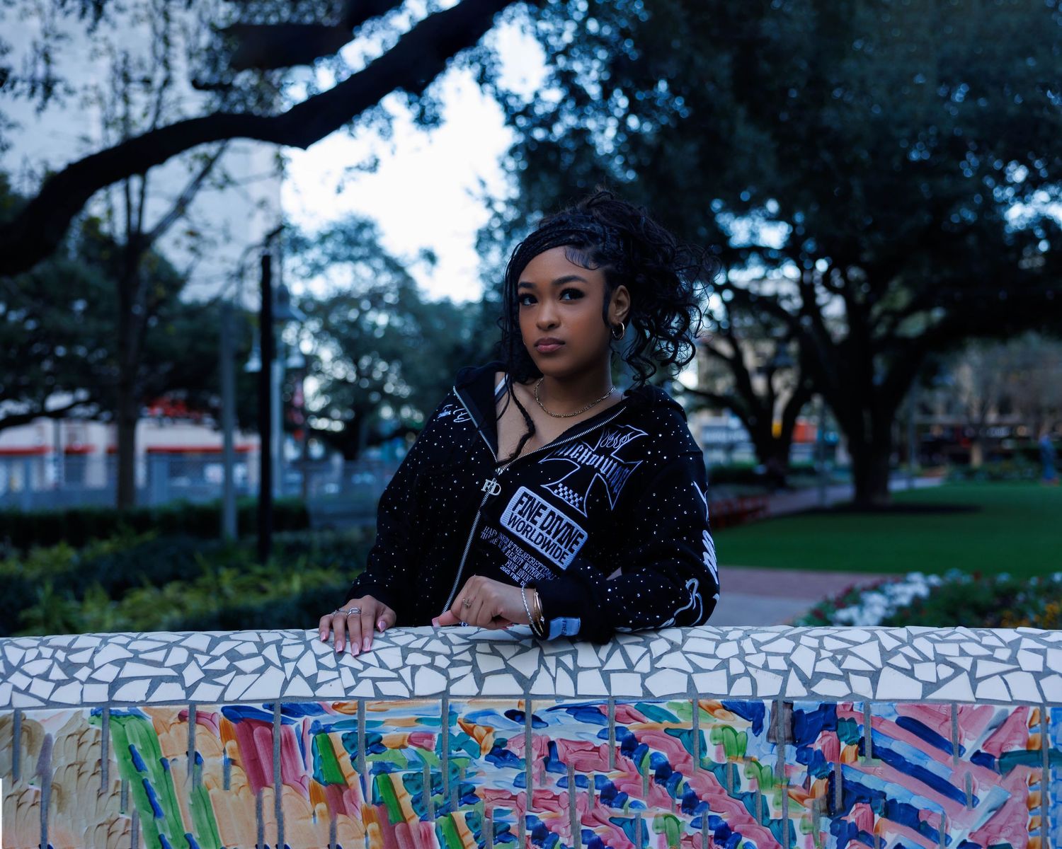 Artistic portrait against colorful graffiti wall with trees in background during blue hour.