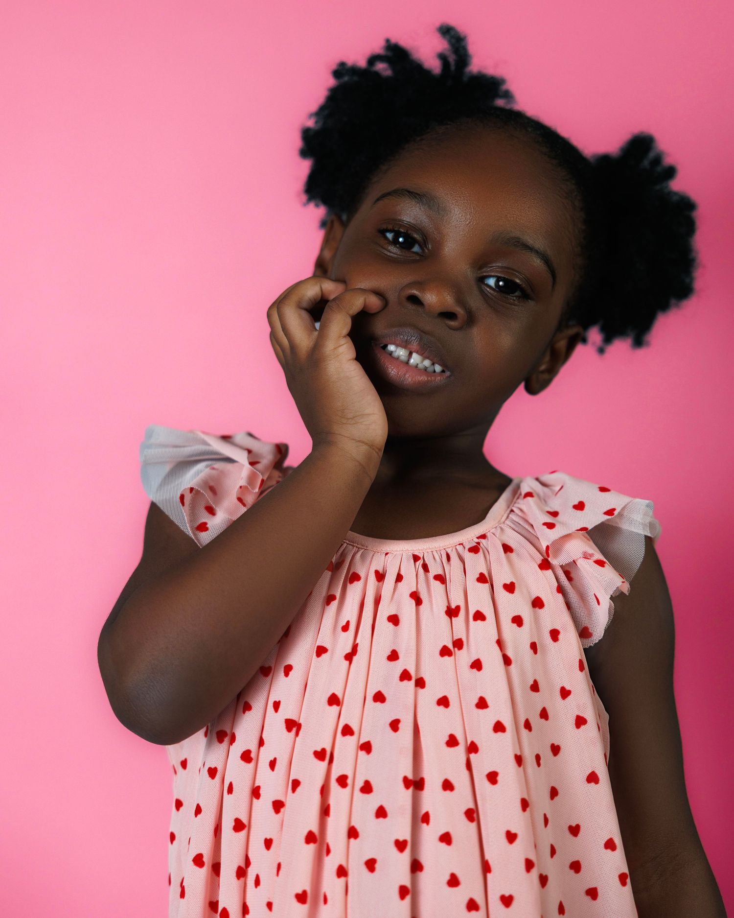 Expressive portrait series of young child in polka dot dress against pink background.