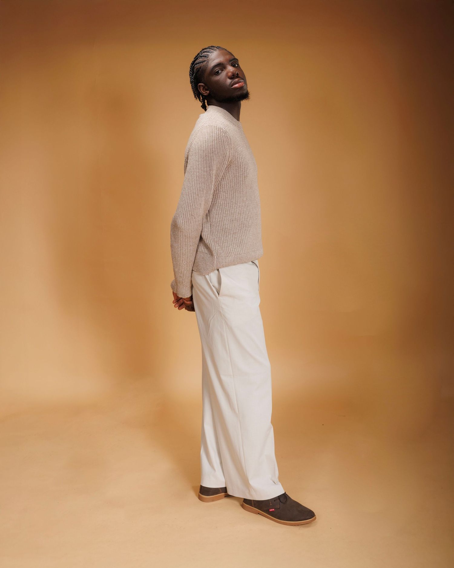 Model wearing a cream colored sweater dress with ribbed texture against a warm brown studio backdrop.