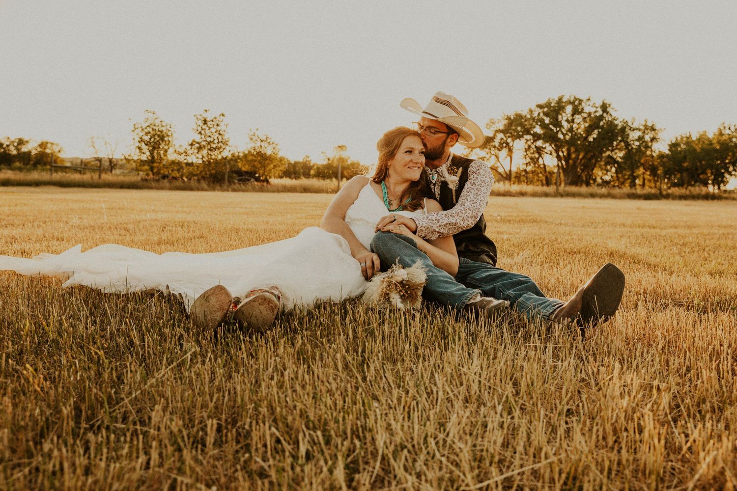 Sunset wedding in South Dakota. Couple in wedding attire sitting in field.