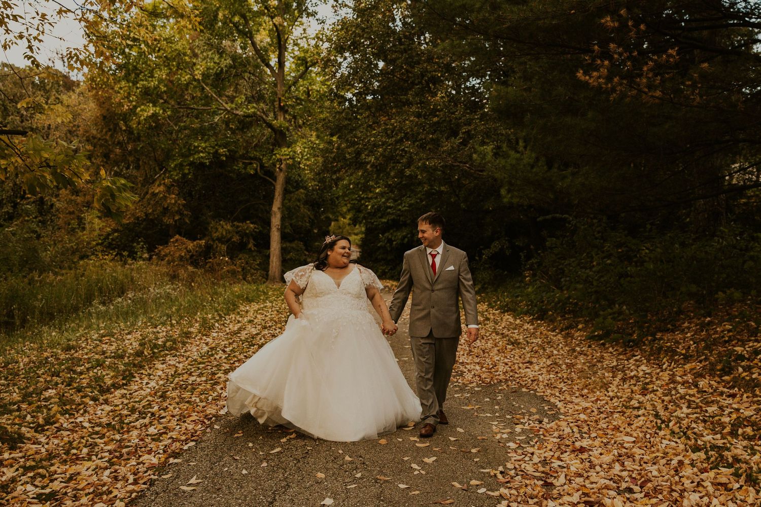 Fall micro-wedding at botanical garden in Toledo. Couple in wedding attire walks through falling leaves.