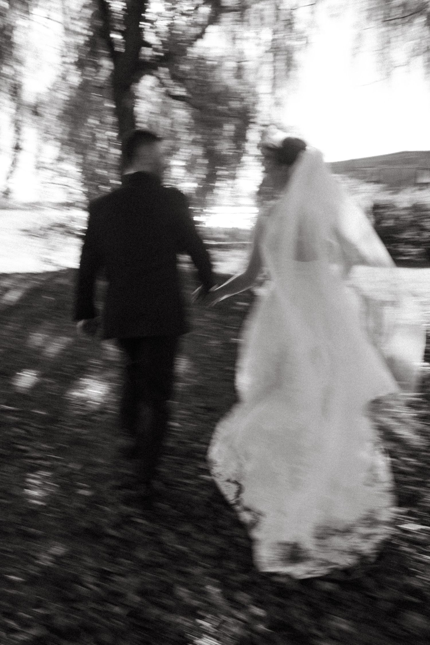 Black and white artistic photo of a bride and groom walking through a misty forest path on their wedding day.