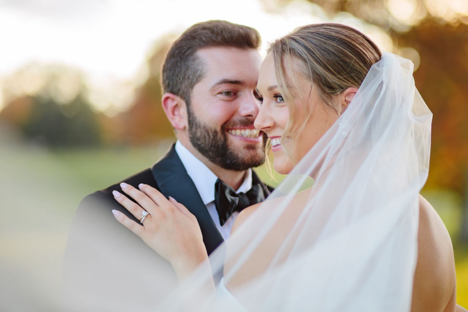 A close affectionate moment between newlyweds captured outdoors during golden hour with a flowing white veil.