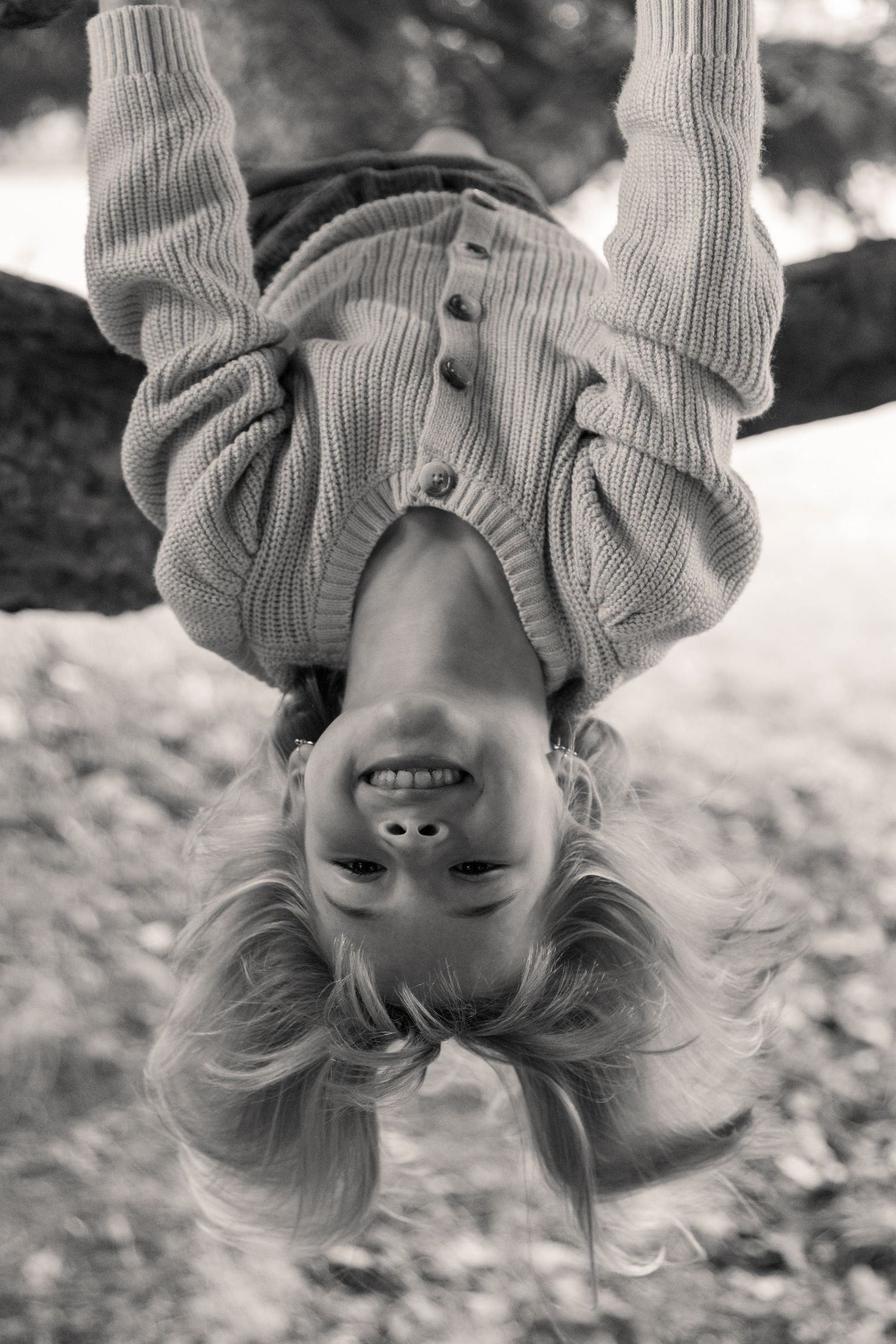 Black and white photo of a girl hanging upside down with her hair falling towards the ground.