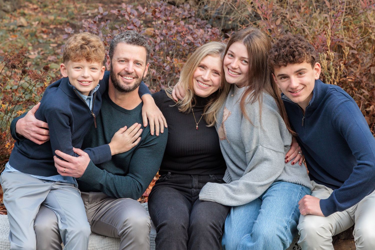 Family snuggling together on a stone wall. Everyone is smiling at the camera.