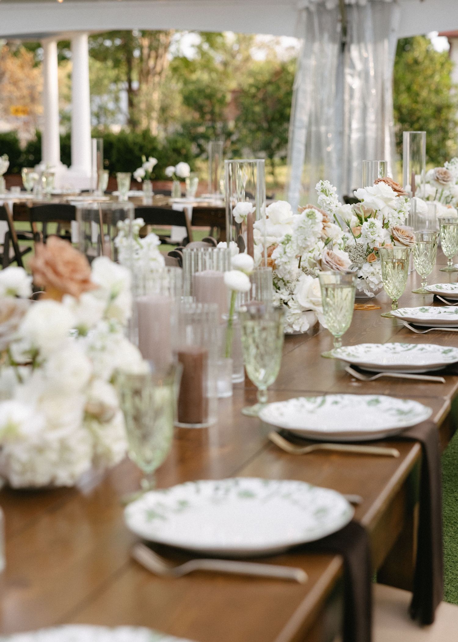 Elegant wedding reception table settings with white floral centerpieces under a tent.