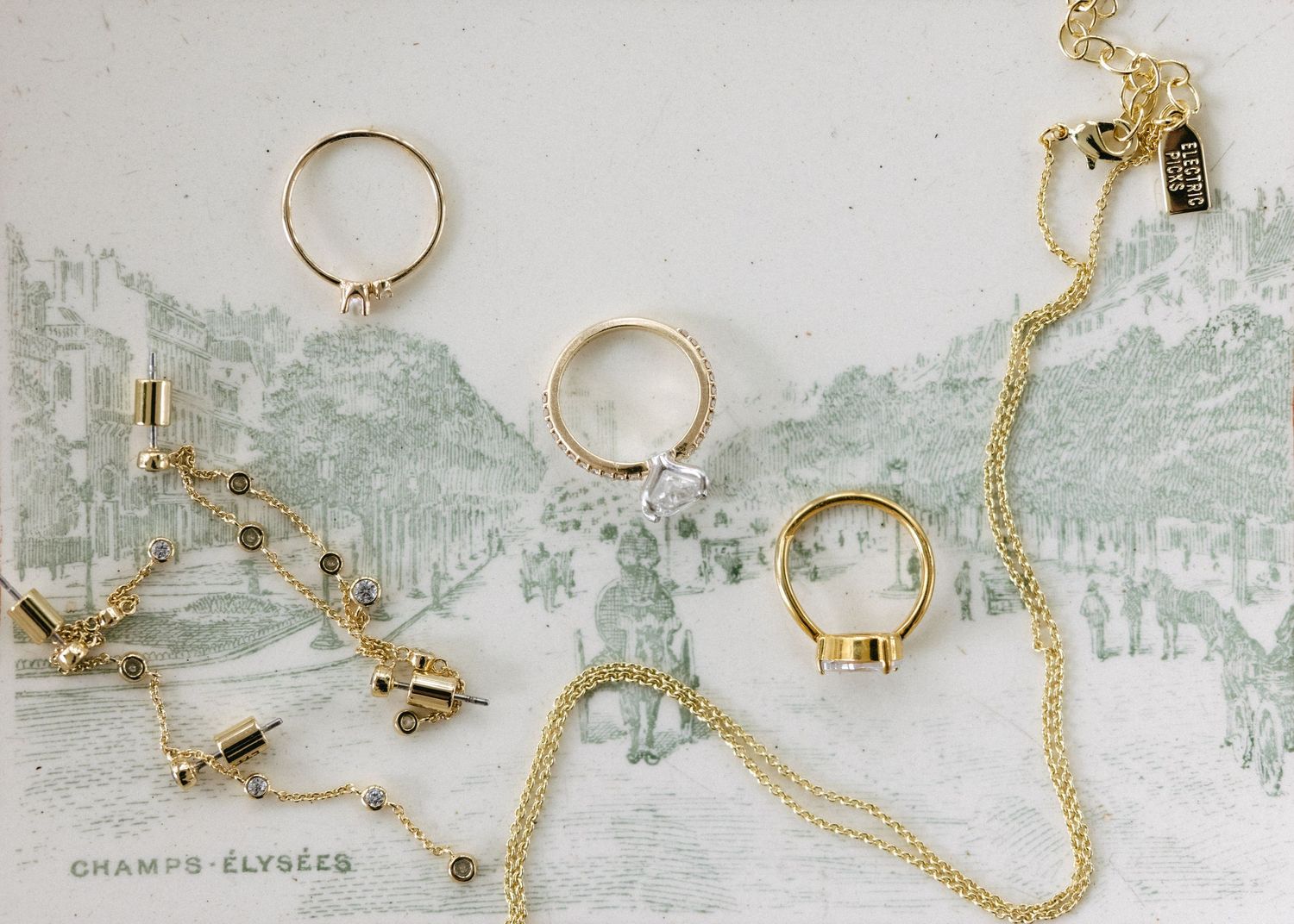 Collection of delicate gold jewelry pieces and rings arranged on a light background.