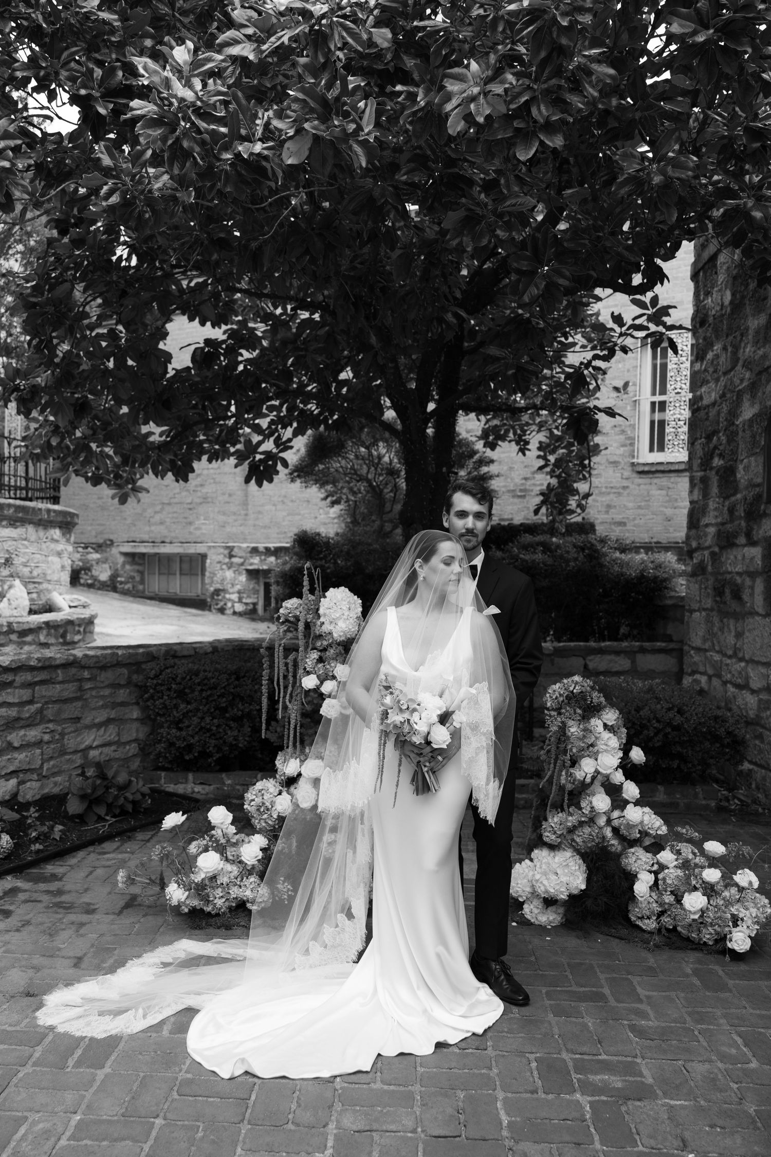 Black and white photo series of a bride in a flowing veil posing in a garden setting with stone walls.