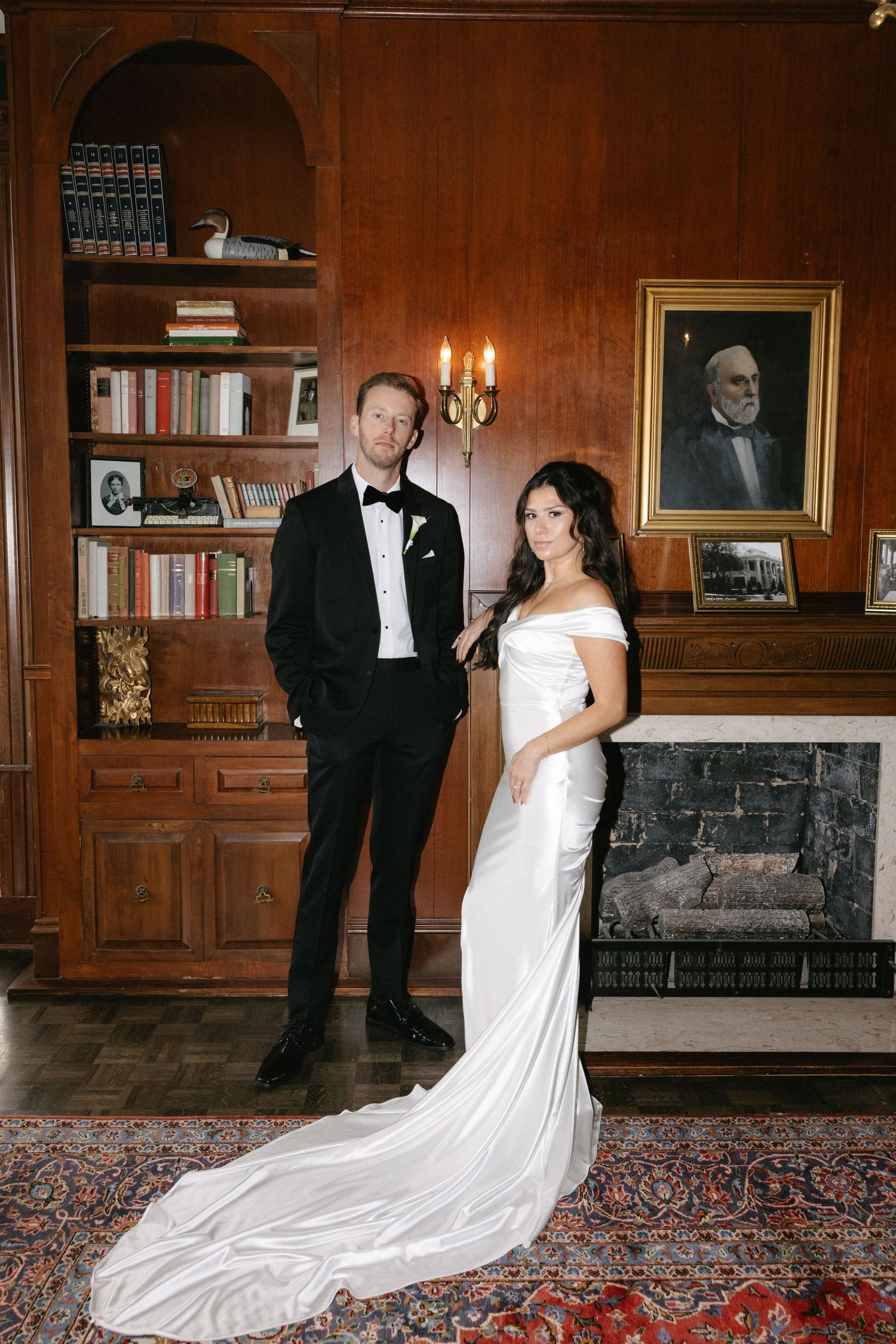 Elegant wedding photos in a wood-paneled library room with fireplace and bookshelves.