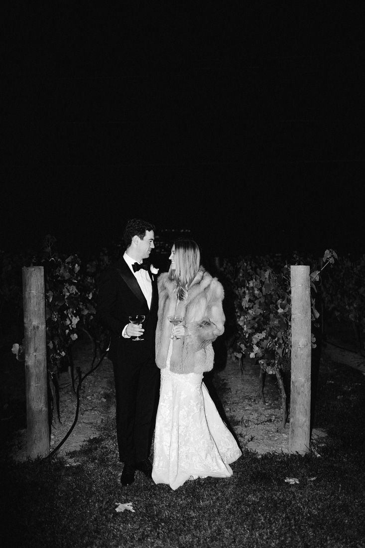 Couple shares romantic moment among vineyard posts during nighttime wedding photography.