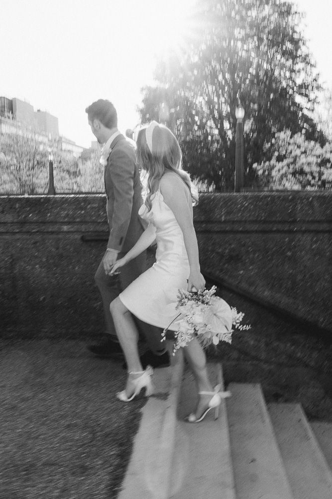 Black and white image of a couple ascending stone steps in formal wedding attire.
