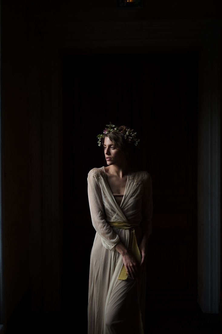 Moody portrait in a flowing cream dress and floral crown with dramatic side lighting.
