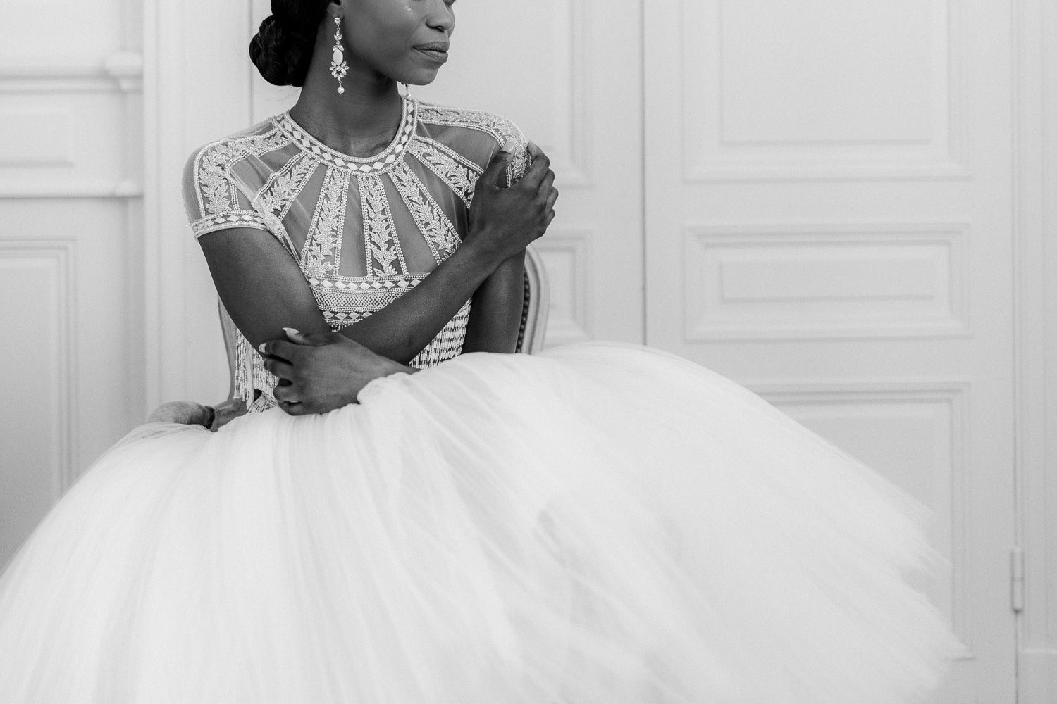 Black and white photo of a bride in a tea-length dress with detailed bodice sitting elegantly.