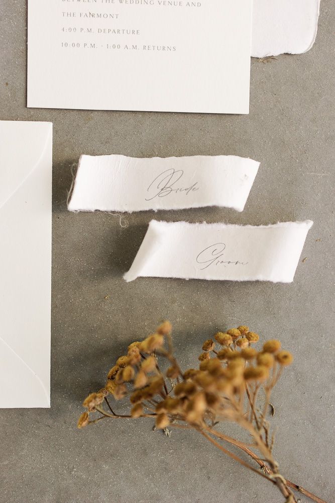 Close-up of wedding stationery with dried golden flowers and torn paper name tags.