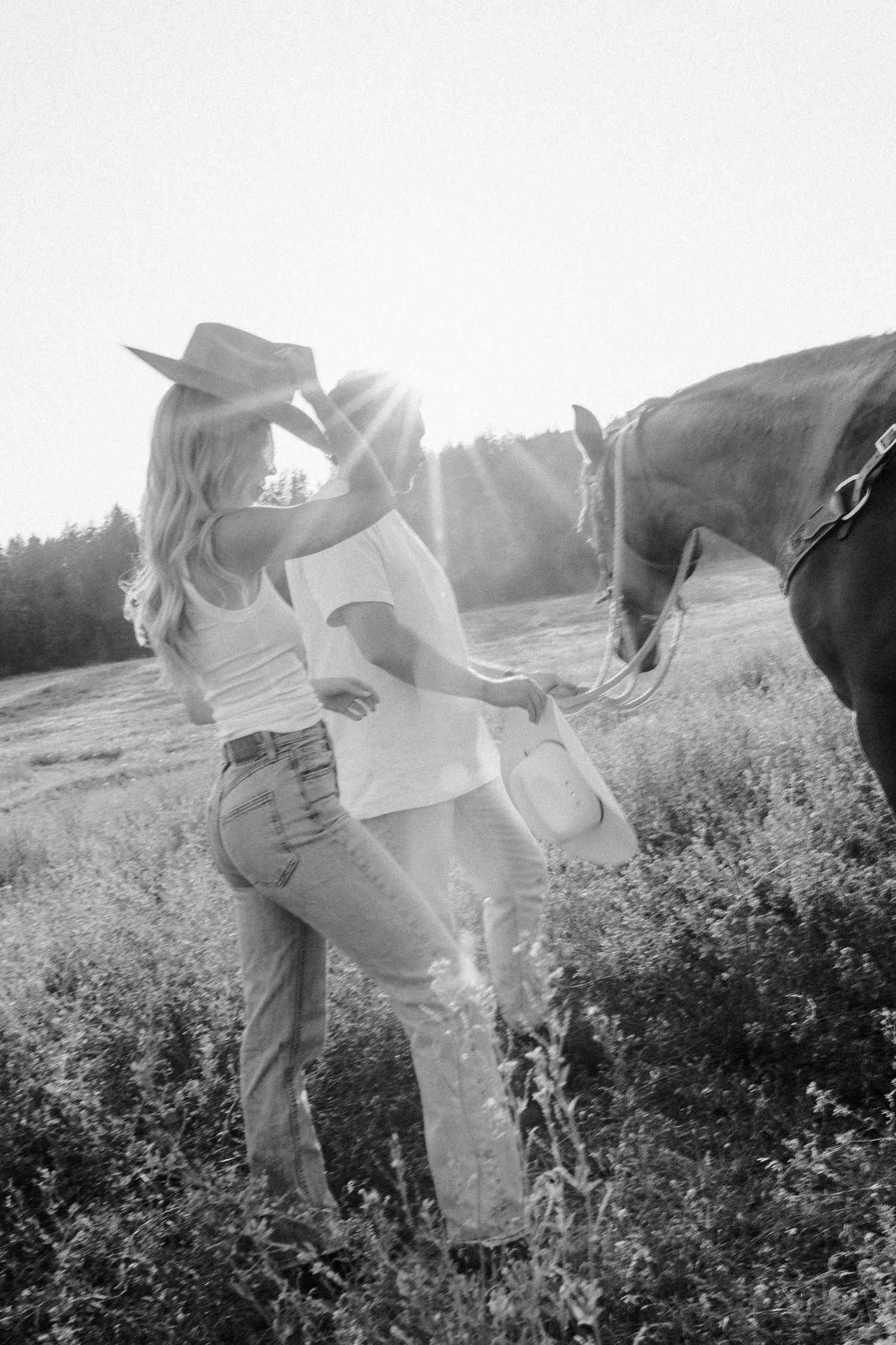 Black and white photo of people with horses in a misty field at sunset.