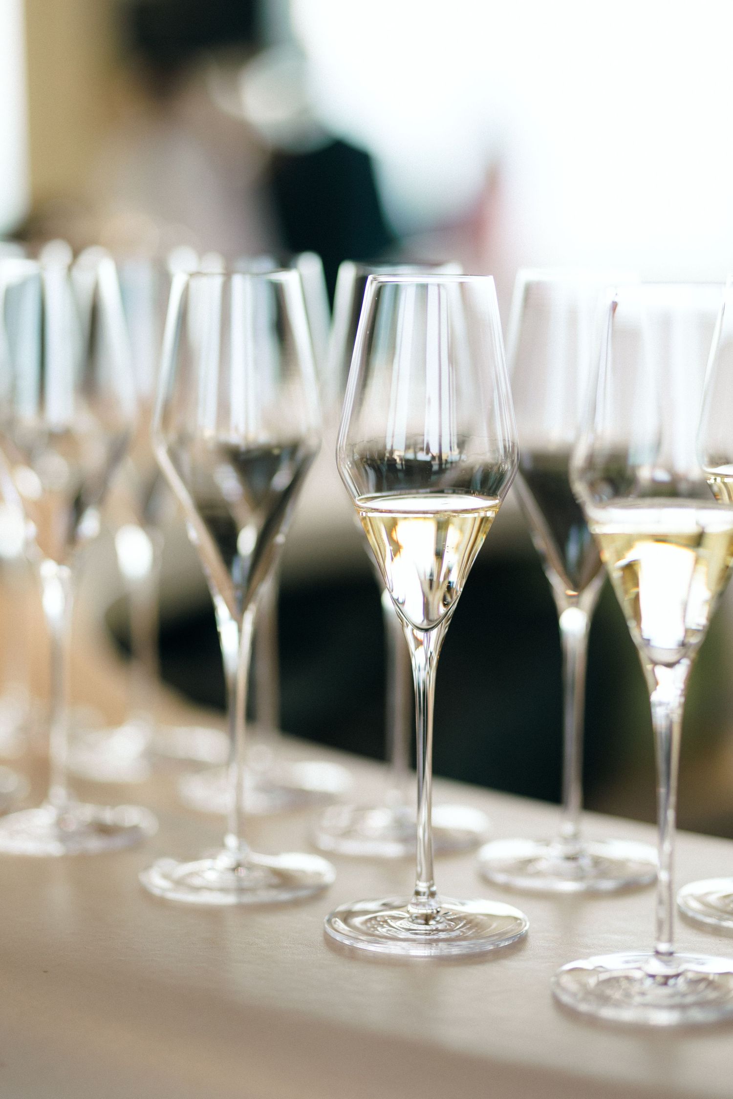 Row of empty champagne flutes lined up on a white tablecloth at a formal event.