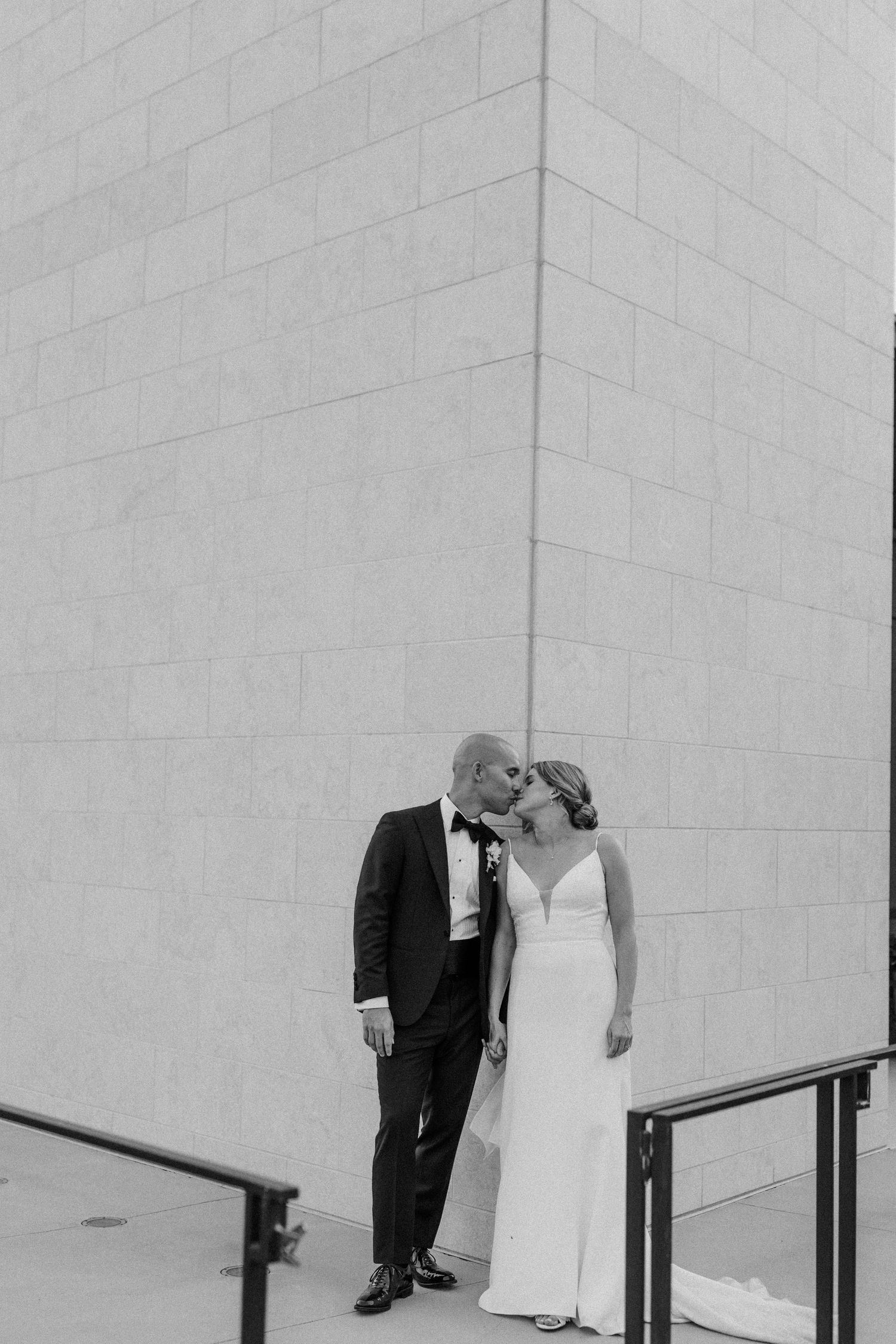 Intimate black and white portrait against a modern architectural wall.