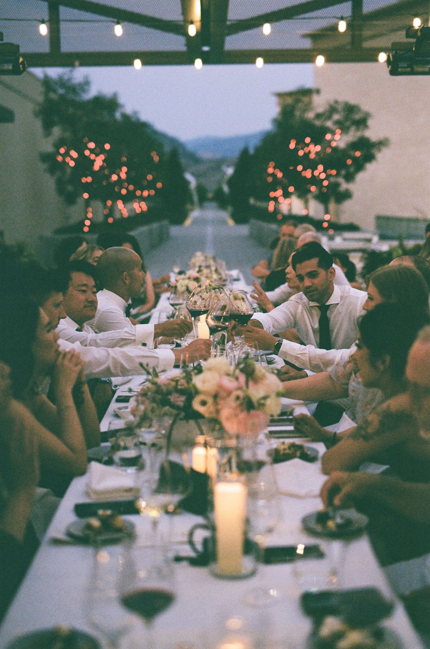 Outdoor wedding reception dinner under string lights at dusk with mountain views.