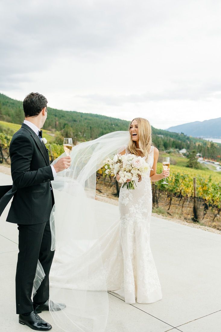 Bride and groom toast with champagne on a terrace overlooking vineyards and mountains.