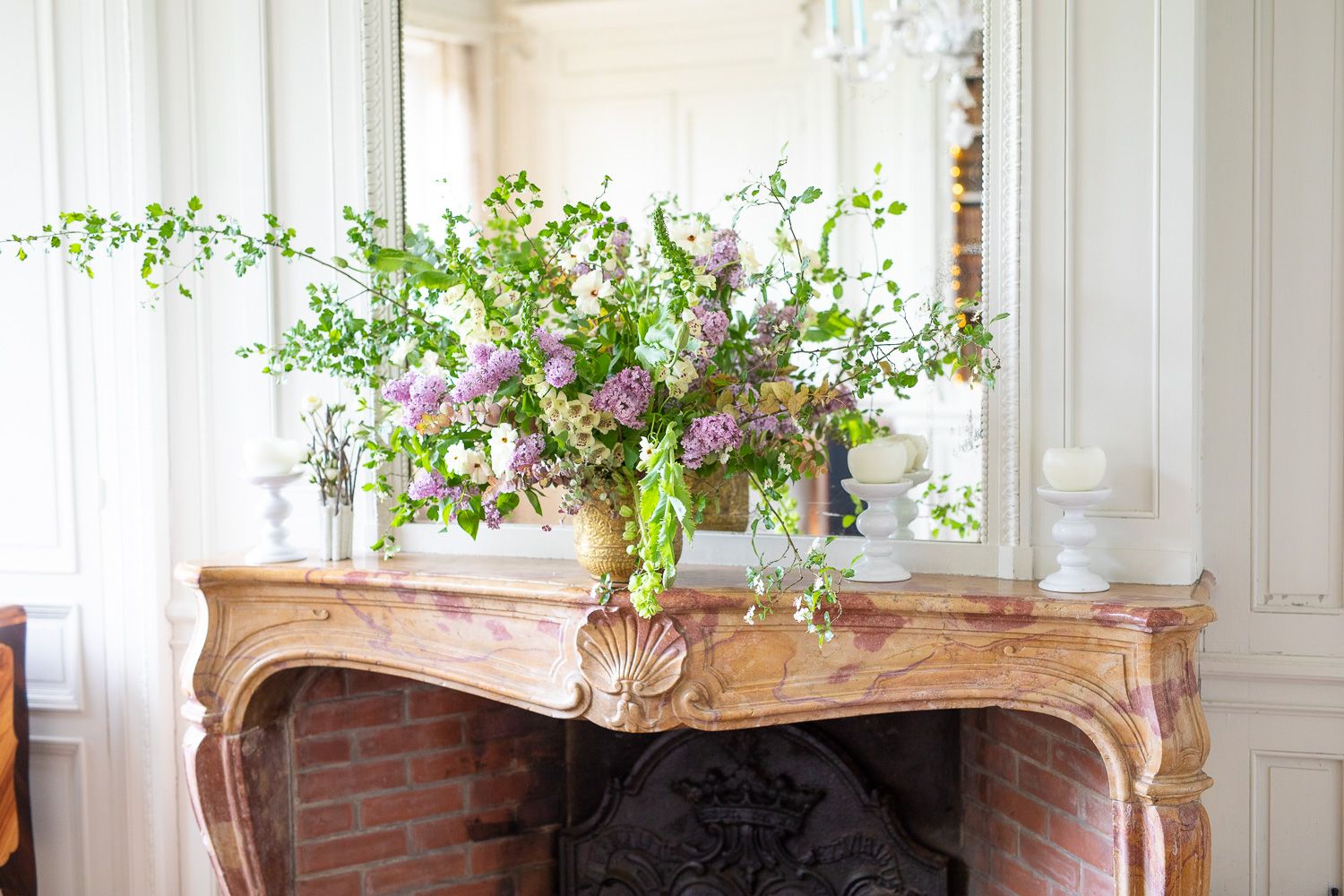 Elegant floral arrangement with pink and purple blooms on ornate marble fireplace mantel.