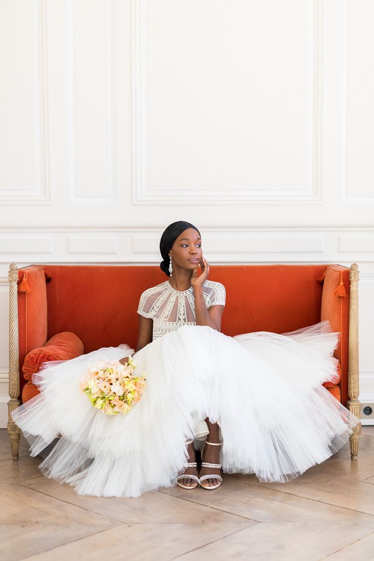 Elegant bridal portrait on coral settee with tulle gown and delicate floral bouquet.