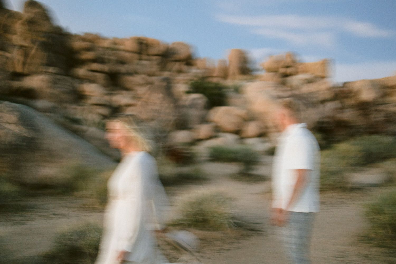 Artistic blurred photo of two people in white clothing against desert rock formations.