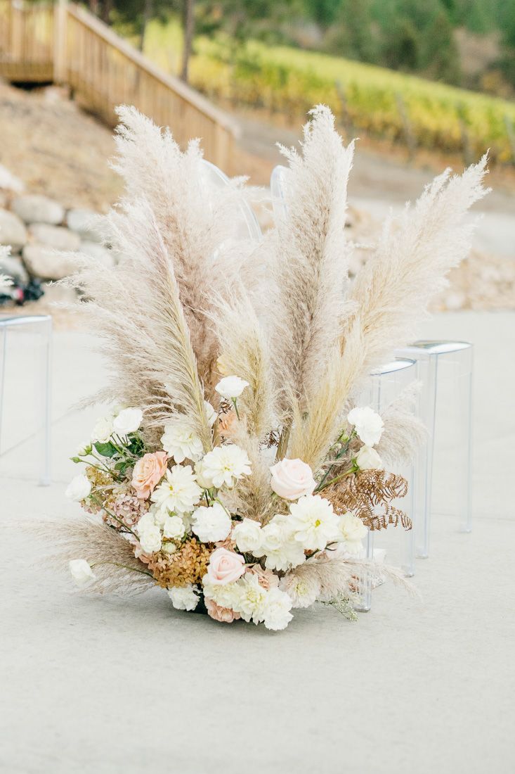 Romantic floral arrangement featuring pampas grass and white blooms on concrete surface.