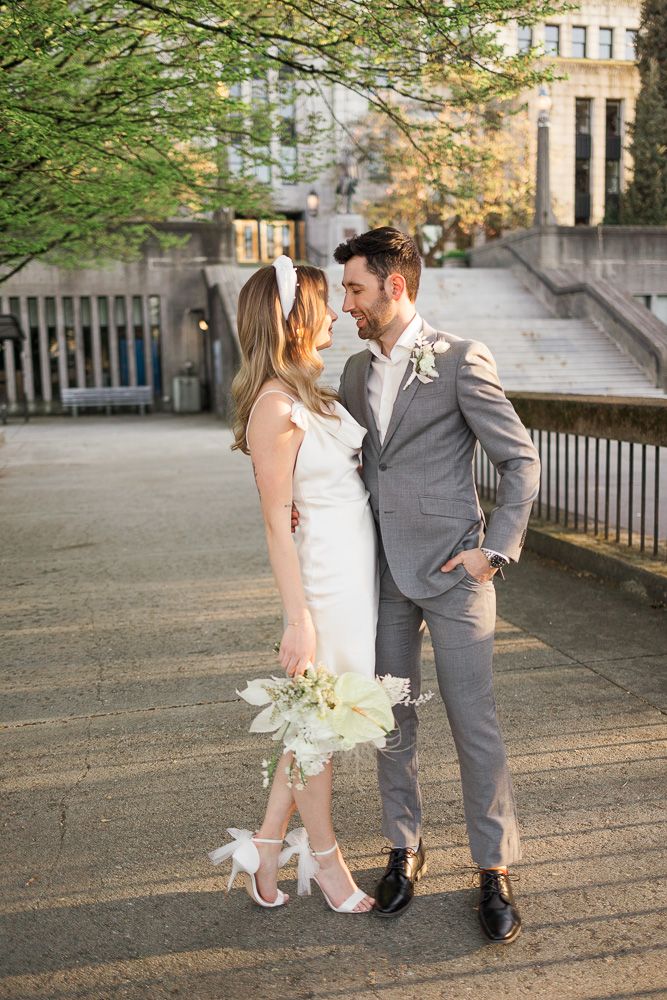 Romantic wedding portrait of a couple in white dress and gray suit against urban architecture.