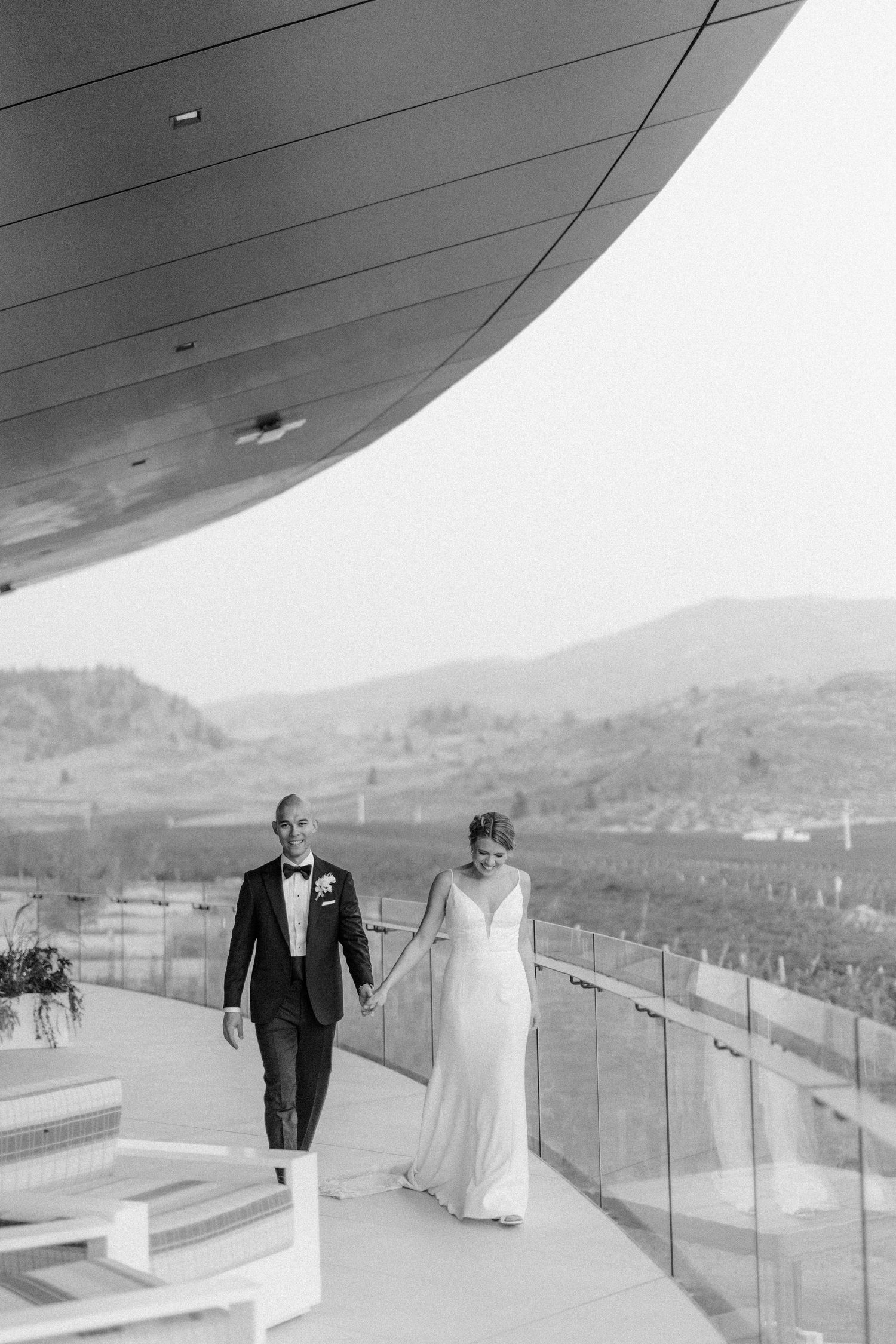 Couple walking along modern curved balcony with mountain landscape views.