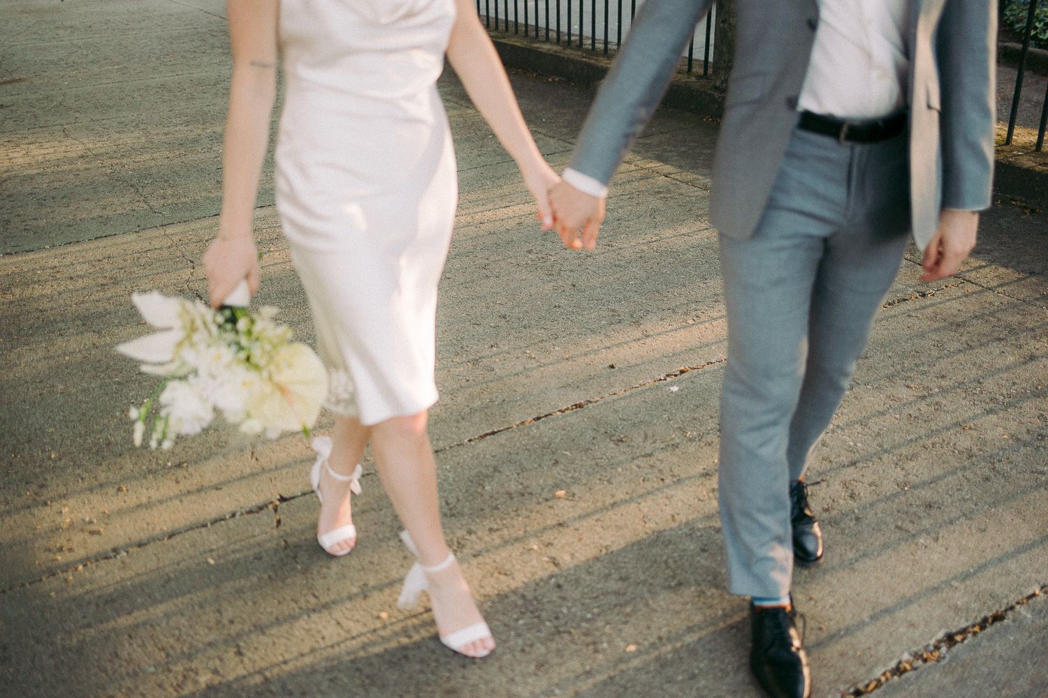 Close up of couple's feet walking together with bride in white dress holding small bouquet.