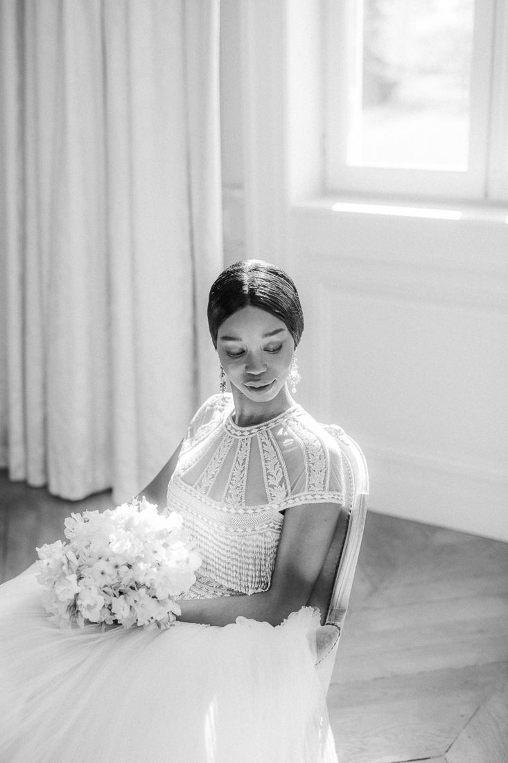 Candid black and white photo of bride in high-neck lace gown holding bouquet.