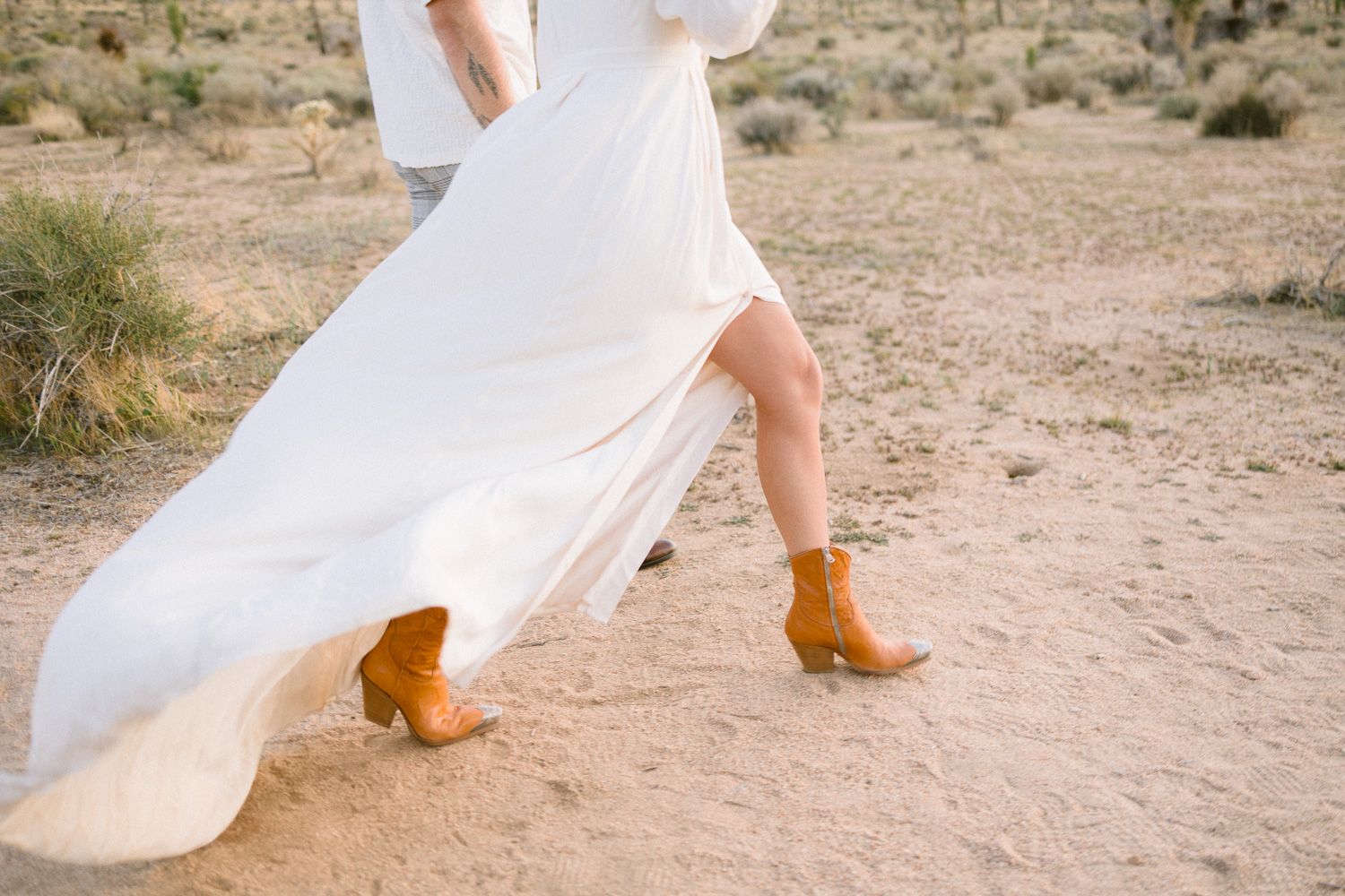Tan boots and flowing white dress hem against desert sand background.