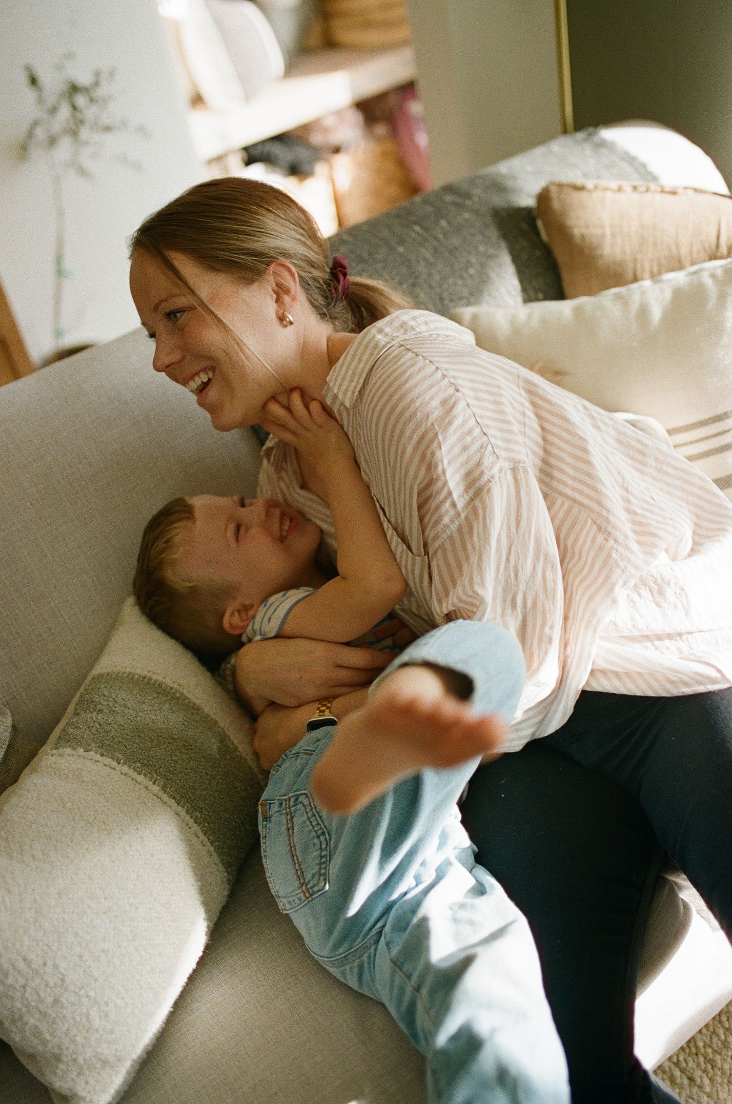 A touching moment of playful bonding and laughter on a comfortable white couch in a sunlit living room.