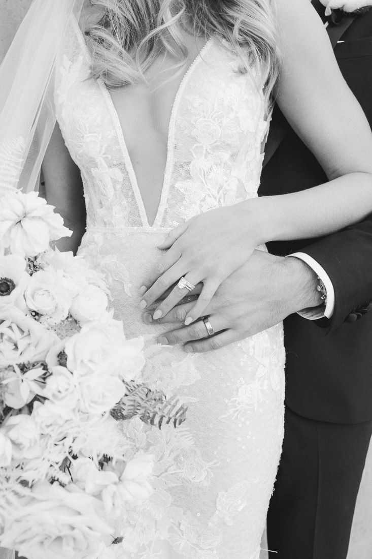 Close-up black and white photo of wedding rings and bouquet details.